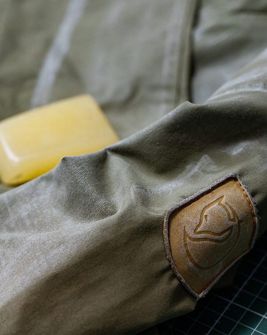 A close‑up of a green fabric with a leather patch featuring a logo, alongside a yellow bar of soap.